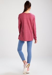 Červený dlouhý rukáv s volným střihem a kulatým výstřihem, v kombinaci se světle modrými skinny džíny a růžovými teniskami.