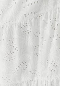 Tissu blanc brodé présentant des motifs floraux et de feuilles, avec des détails découpés et une texture froncée en bas.