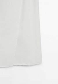 Partie inférieure d'une jupe en tissu blanc avec un ourlet brut et effiloché sur un fond blanc.