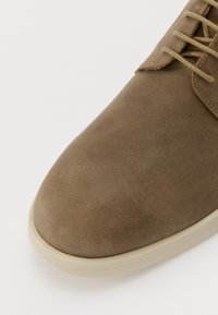Brune semsket sko med en rund tå, lys såle og flate lisser. Har en jevn tekstur med minimale sømdetaljer.