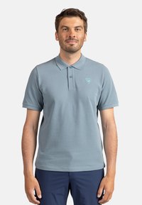 Polo shirt azzurro chiaro con due bottoni, maniche corte e un piccolo logo sul petto. Tessuto in cotone morbido, vestibilità casual e superficie liscia.