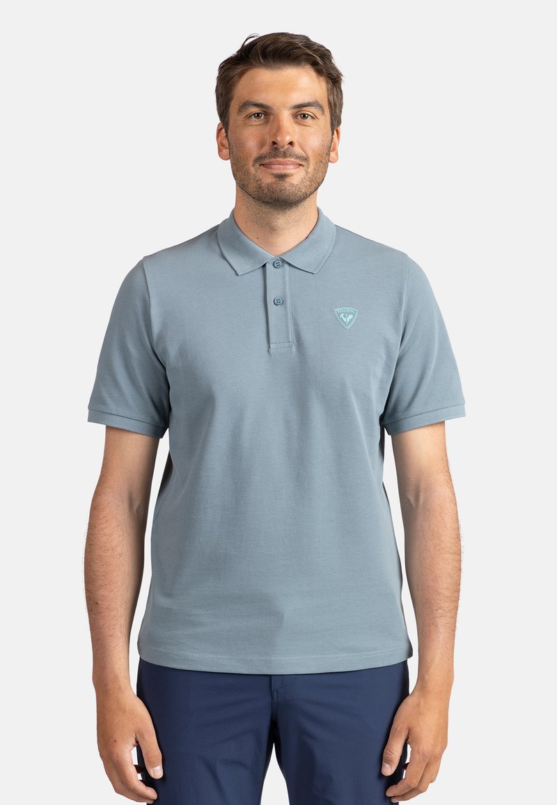 Polo shirt azzurro chiaro con due bottoni, maniche corte e un piccolo logo sul petto. Tessuto in cotone morbido, vestibilità casual e superficie liscia.