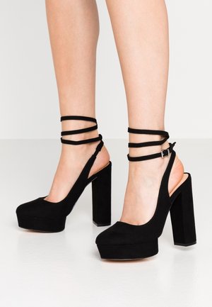 Schwarze Plattform-High Heels aus Wildleder mit Slingback-Design und Knöchelriemen. Die Schuhe haben dicke, rechteckige Absätze und abgerundete Zehen.