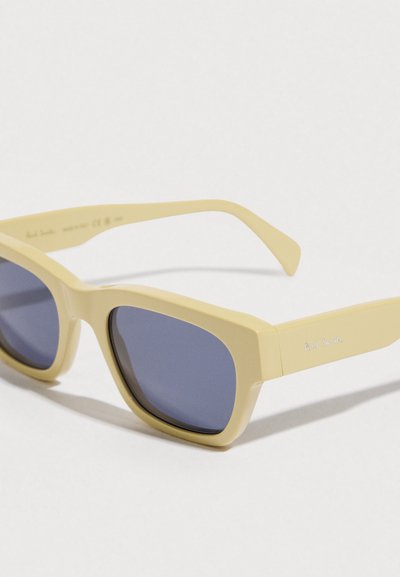 Gafas de sol de plástico amarillo con montura rectangular, lentes azul oscuro y un detalle sutil del logo en la patilla. Acabado suave y mate.