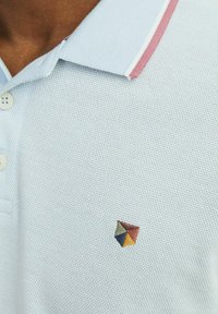 Polo shirt azzurro chiaro con tessuto strutturato, dotato di una patta con due bottoni e un colletto con strisce rosa e bianche. Logo geometrico ricamato.