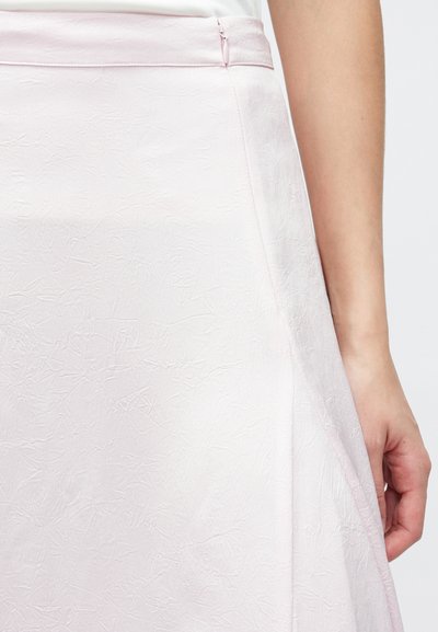 Světlounce růžová sukně s texturovaným povrchem, hladkým pasovým lemem a bočním zapínáním na zip. Látka má mačkaný vzhled.