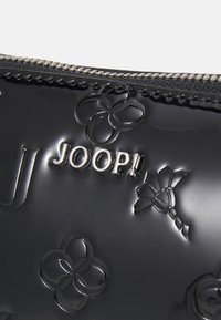 Pochette in pelle verniciata nera con motivo floreale in rilievo e logo "JOOP!" in tonalità argento. Presenta una chiusura con zip sul'A parte superiore e dettagli testurizzati.