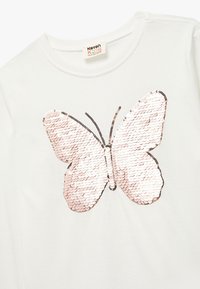 Hvid T-shirt med et stort, pailletbesat sommerfugledesign i pink og sølv nuancer. Sommerfuglen har tydelige sorte konturer og en glitrende tekstur.