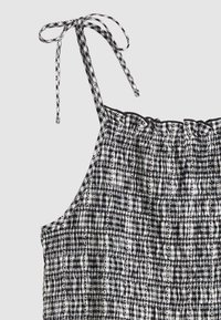 Αμάνικη μαύρη και λευκή καρό μπλούζα με ζώνες που δένουν και διακριτικές λεπτομέρειες από δαντέλα.