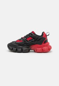 Schwarze und rote Sneaker mit einer strukturierten Oberfläche, Mesh-Details und dicken, gepolsterten Sohlen, die von Schwarz nach Rot übergehen.