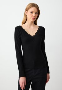 Langärmliges, figurbetontes schwarzes Oberteil mit V-Ausschnitt und Spitzenbesatz. Hergestellt aus geripptem Stoff, der eine feine Textur und ein elegantes Design aufweist.