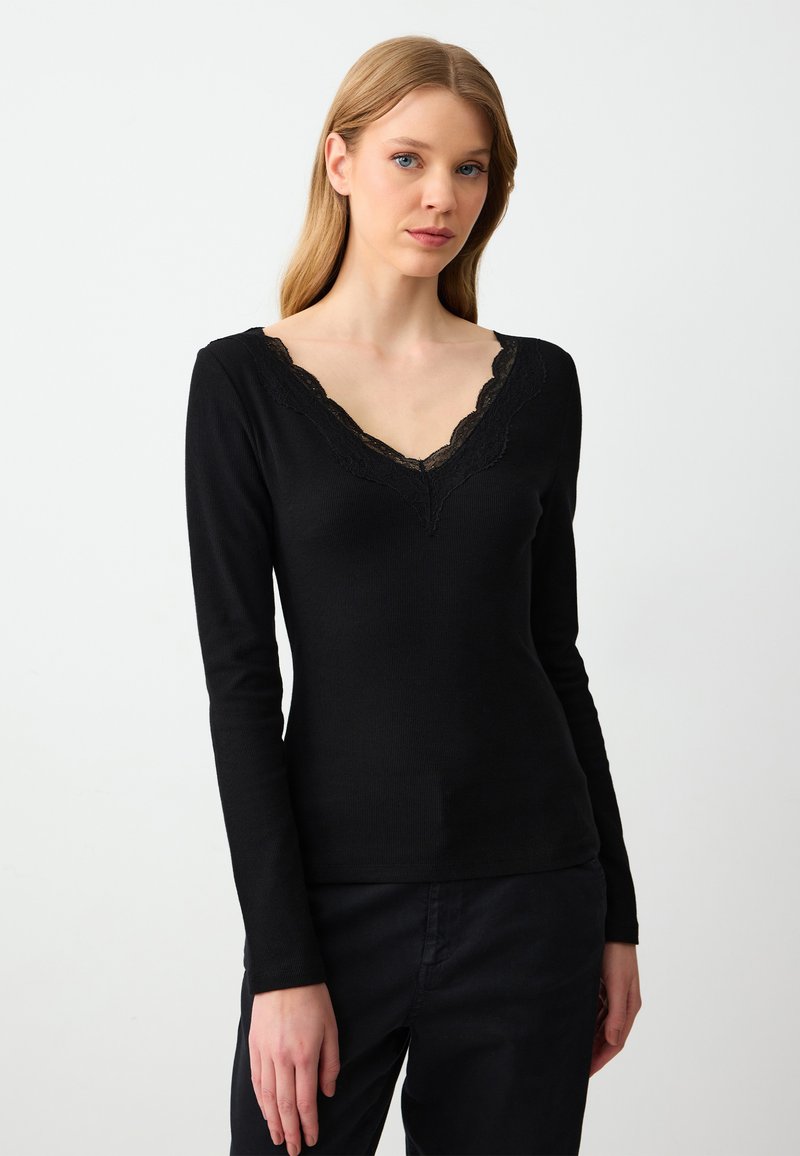 Langärmliges, figurbetontes schwarzes Oberteil mit V-Ausschnitt und Spitzenbesatz. Hergestellt aus geripptem Stoff, der eine feine Textur und ein elegantes Design aufweist.