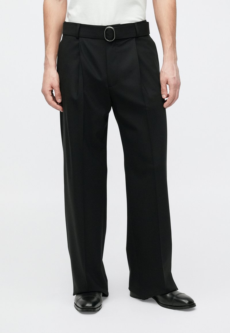 Pantaloni neri su misura con una cintura caratterizzata da una fibbia metallica circolare, piega frontale e design a gamba larga. Tessuto dalla texture liscia.