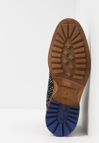 Semelle d'une chaussure pour hommes avec une bande de roulement en caoutchouc beige et bleu, un motif de grip texturé, et les indications de taille "7 H" visibles au niveau du talon.