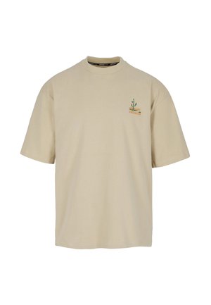 Beiges T-Shirt mit kurzen Ärmeln, auf der oberen linken Brust befindet sich eine kleine grüne Kaktus- und orangefarbene Grafik.