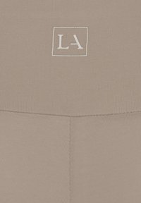 Beige leggings featuring a smooth texture and a subtle stitched design, with a white embroidered "LA" logo in a square outline.