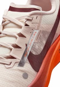 Nærbillede af Nike trail racing sko med beige snørebånd, geometrisk tekstureret stof, orange og burgundy sål samt "VaporWene" mærke.