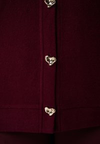Bordeaux wol stof met een gladde textuur, voorzien van hartvormige gouden knopen langs de voorkant. Eenvoudig ontwerp, geen patronen.