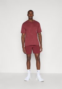 Bordeaux t-shirt en shorts set, gemaakt van katoen met een zachte textuur. Bevat een ronde hals en een klein logo op de borstzak van de t-shirt.