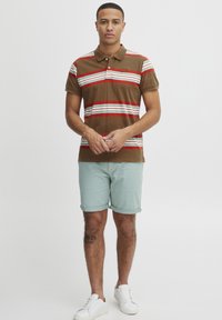 Brun polo skjorte med røde og hvide vandrette striber, korte ærmer og krave, parret med lyseblå shorts og hvide sneakers.