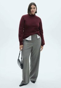 Bordeauxfarbener Strickpullover mit hohem Kragen, kombiniert mit hellgrauen weiten Hosen. Accessoires sind eine kleine schwarze Handtasche und spitze Schuhe.