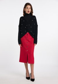 Maglione nero lavorato a maglia con dettagli in perle, design attorcigliato, abbinato a una gonna midi rossa a costine con bottoni frontali e uno spacco. Tacchi neri.
