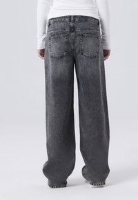 Široke traperice u izblijedjelom crnom denimu. Imaju dva stražnja džepa i vidljive šavove. Mekana tekstura s opuštenim krojem.