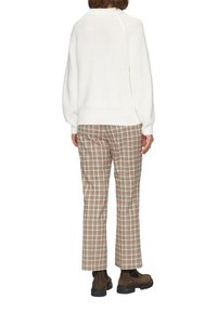 Witte gebreide trui met een losse pasvorm en geribbelde manchetten, gecombineerd met beige geblokte broek met rode en zwarte accenten. Bruine enkellaarzen maken de look compleet.