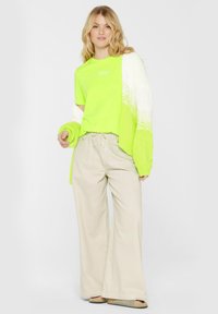 Neon green t-shirt paired with an oversized white and lime green knit cardigan, beige wide-leg pants, and olive green sandals.