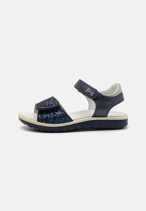 Sándalo infantil azul marino con tira frontal brillante, correa ajustable en el tobillo, plantilla blanca acolchada y suela negra resistente.