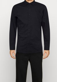 Černá košile s dlouhým rukávem z bavlny, s knoflíkovou légou, měkkou texturou a klasickým límcem. Doplněná černými kalhotami.