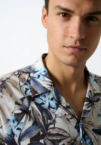 Kurzärmliges Hemd mit floralem Muster in Blau- und Brauntönen. Hergestellt aus leichtem Stoff, verfügt es über einen klassischen Kragen und eine lockere Passform.