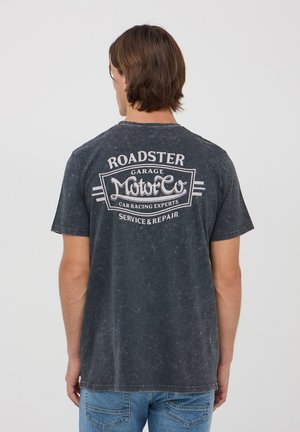 Szara koszulka z krótkimi rękawami z białym nadrukiem z tyłu. Nadruk zawiera napis "ROADSTER GARAGE MotorCo" oraz elementy graficzne.