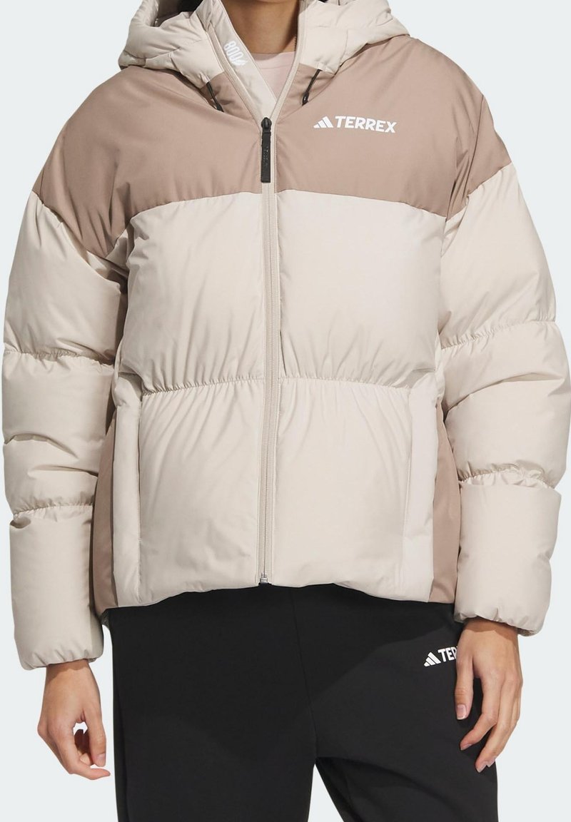 Veste matelassée beige et marron clair à blocs de couleurs avec capuche et logo TERREX, portée avec un pantalon TERREX noir.