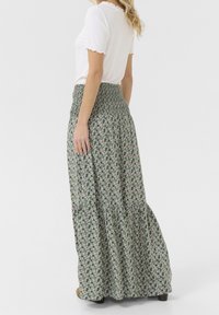 Maxiskirt i grøn med små blomster mønstre, samlet talje, og lagdelt design. Materialet er letvægts med en flydende tekstur.