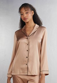 Satinpajamaströja i ljusbeige med svarta detaljer. Har långa ärmar, knappframsidan och krage. Slät, glansig yta.