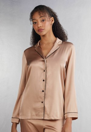 Satin pajama top in light beige with black piping. Features long sleeves, a button-down front, and a collar. Smooth, glossy texture.