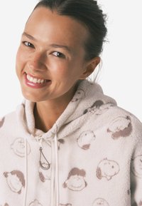 Fuzzy creme hoodie med brunt tegneserie-sheep mønster, med lynlås foran og snoretræk i hætten. Blød tekstur og afslappet pasform.