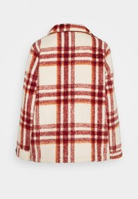 Oversized kappa i ullblandning med en krämfärgad bas och rödorange rutmönstring. Inkluderar en notched krage och mjuk textur.