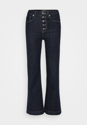 Tamsiai mėlynos aukšto liemens platėjančios džinsinės kelnės su penkiais sidabriniais mygtukais priekyje ir kontrastingomis siūlėmis aplink kišenes bei siūles.