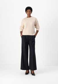 Maglione a cable knit crema con maniche lunghe, abbinato a pantaloni a vita alta neri a gamba larga e tacchi neri lucidi. Design semplice e strutturato.