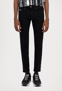 Črni denim kavbojke s slim fit krojem, petimi žepi in zlatimi gumbnimi poudarki. Nosi se z črnimi supergami, ki imajo izrazit bel napis.