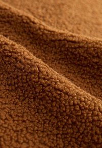 Brauner, strukturierten Stoff mit einer weichen, flauschigen Oberfläche, die ein dichtes Boucle-Muster aufweist und ein warmes, gemütliches Aussehen erzeugt.