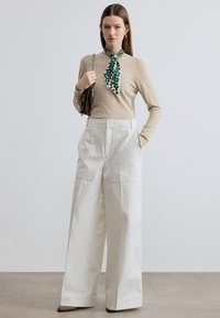 Μπεζ πλεκτό τοπ συνδυασμένο με λευκό παντελόνι φαρδιάς γραμμής με τσέπες μπροστά, πράσινο φλοράλ φουλάρι και ασημένια τσάντα χειρός.