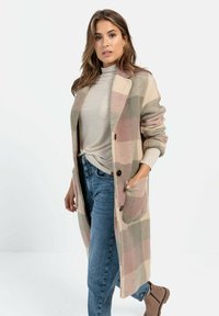 Beige en roze geruite lange cardigan gemaakt van zachte stof met een kraag, voorzakken en bruine knopen, gecombineerd met een licht top en jeans.