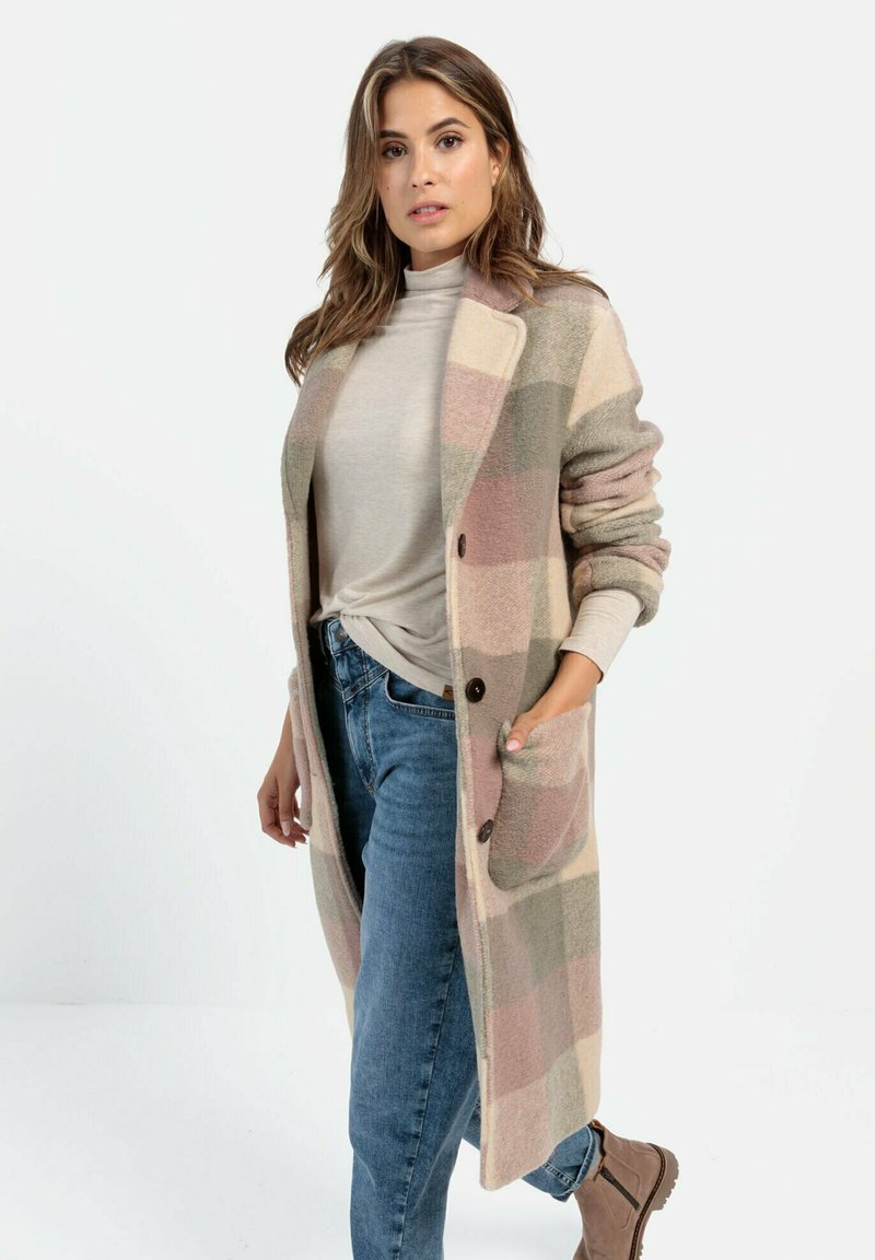 Beige en roze geruite lange cardigan gemaakt van zachte stof met een kraag, voorzakken en bruine knopen, gecombineerd met een licht top en jeans.