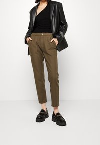 Zwarte textuurtop, oversized zwarte lederen blazer, olijfgroene broek met zakken en stevige zwarte loafers met kettingaccent.