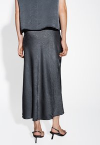 Grijze, textuur heeft een mouwloze top gecombineerd met een lange, vloeiende grijze rok. Strappy zwarte hakken maken de outfit af. Glad, glanzend materiaal.
