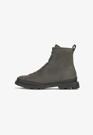 Bottes basses en cuir gris avec bout rond, fermeture à lacets sur le devant et surface texturée. Elles disposent d'une semelle en caoutchouc noire robuste et d'une bride de traction à l'arrière.