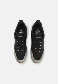 Baskets de sport noires avec une tige texturée, des accents argentés et des semelles en caoutchouc blanc. Elles présentent des lacets et un logo sur la languette.